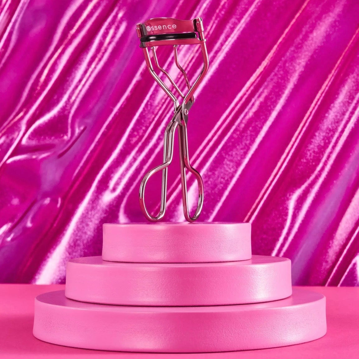 Essence Eyelash curler on a pink platform with a vibrant pink background