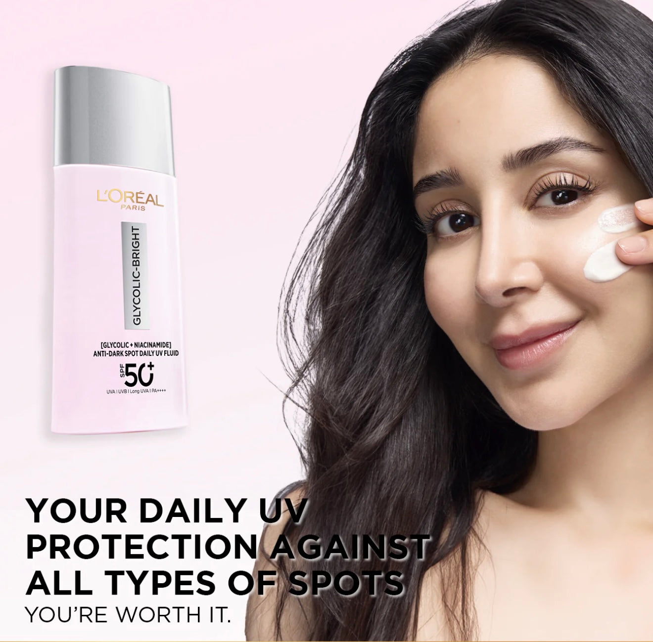 Woman applying cream to her face with L'Oreal bottle on a pink background