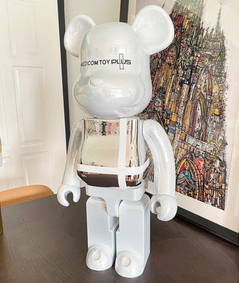 White and silver robot-like figure on a table with a colorful abstract painting in the background