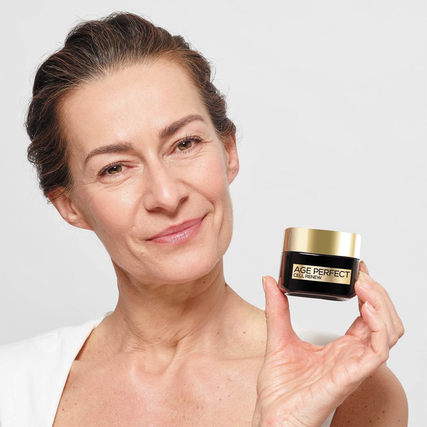 Woman holding a jar of 'Age Perfect' cream against a plain background