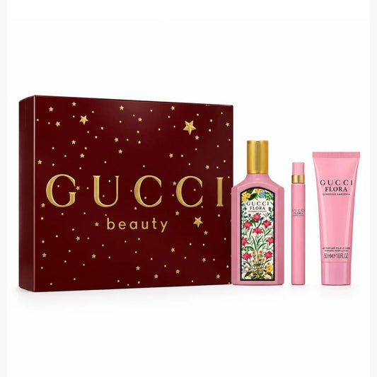 Gucci Flora Gorgeous Gardenia Beauty gift set featuring a dark red box with gold stars and lettering, a pink perfume bottle with a gold cap and floral label, a matching pink travel spray, and a pink body cream tube.