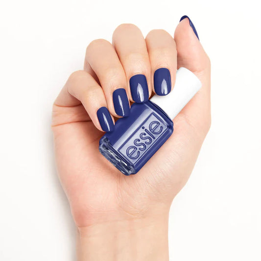 Hand holding an essie nail polish bottle with matching blue nail polish on a white background