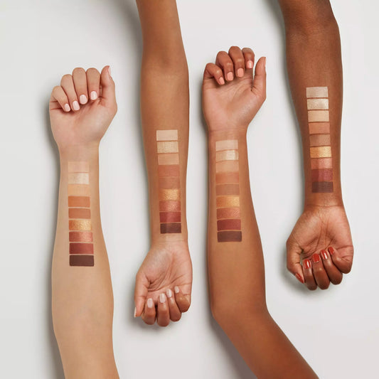 Four arms with different skin tones displaying makeup swatches on a light background of the Essence Brown Edition Eyeshadow palette