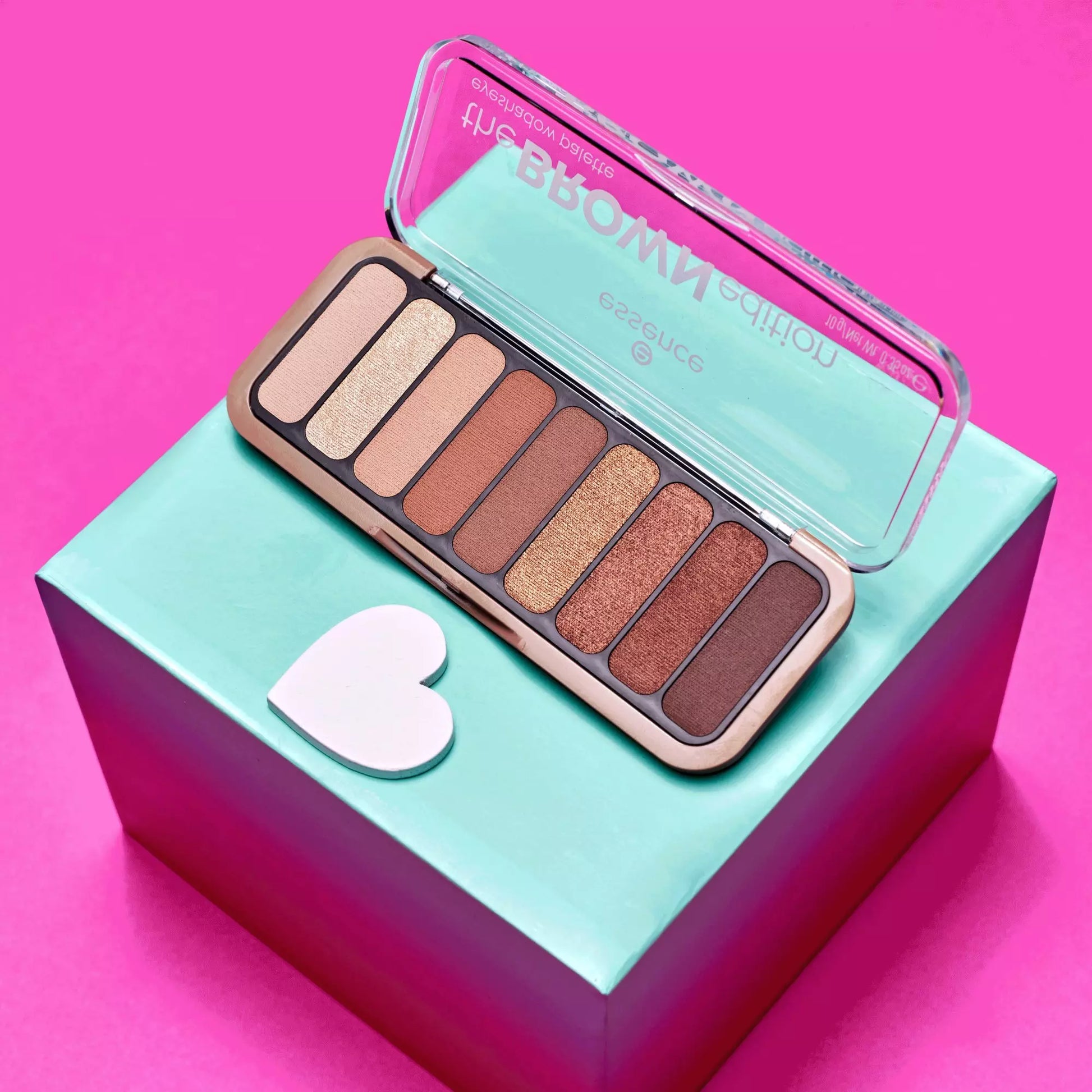 Essence Makeup palette with heart-shaped tool on a turquoise box against a pink background