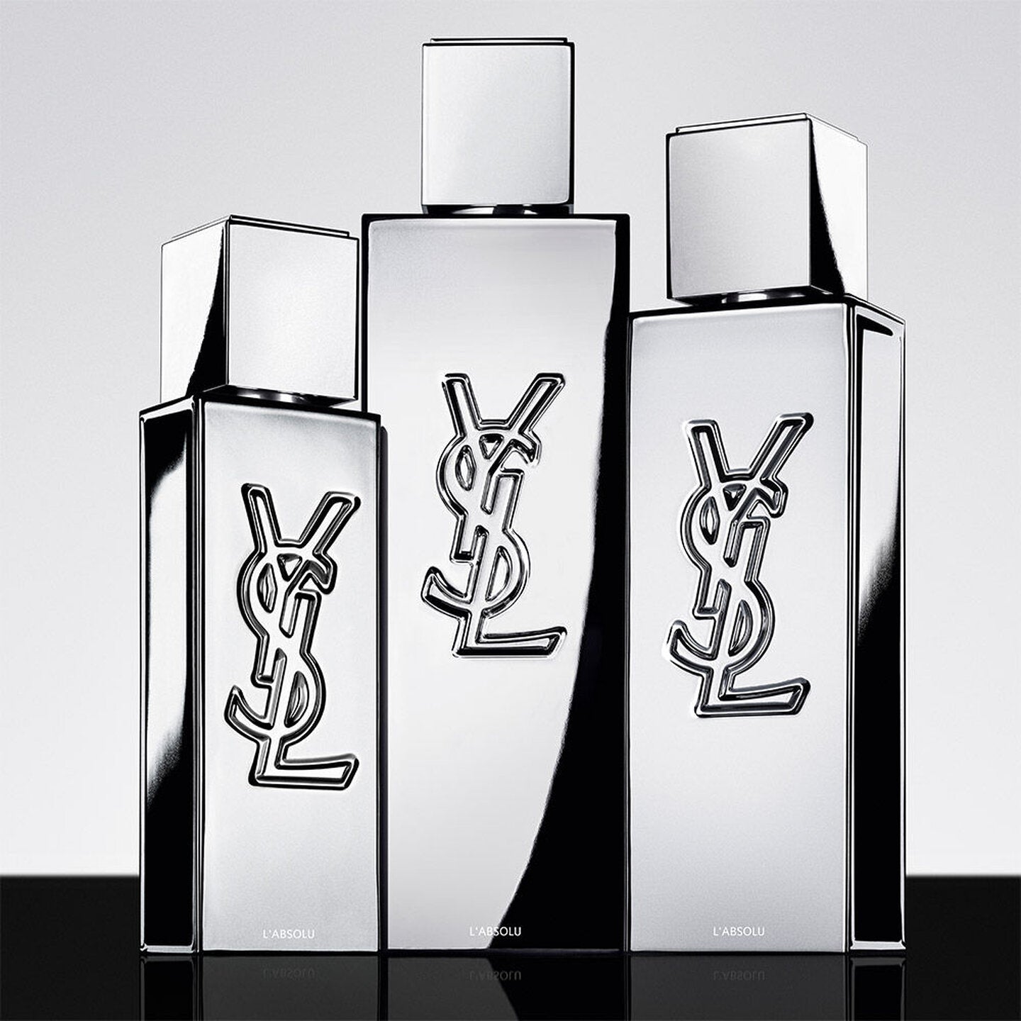 Three silver YSL perfume bottles on a reflective surface with a light gray background
